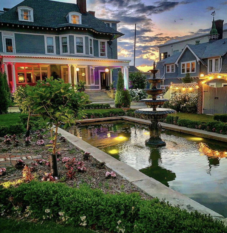 The English gardens and illuminated fountain at 300 Clifton glowing under a twilight sky, a romantic Minneapolis mansion setting after dark.