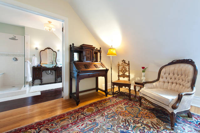 A carved writing desk, armchair and lamp in a guest room at 300 Clifton, with the en-suite bathroom beyond, a quiet spot to work during a Minneapolis business trip.