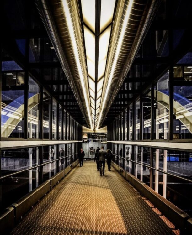 Looking down an enclosed glass skyway bridge over a downtown Minneapolis street, the warm indoor route people use to cross the city on a cold game night.